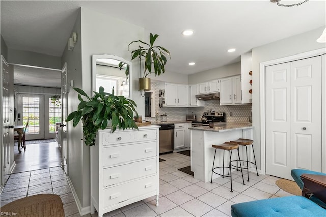 kitchen featuring a peninsula, a kitchen bar, white cabinetry, under cabinet range hood, and stainless steel appliances