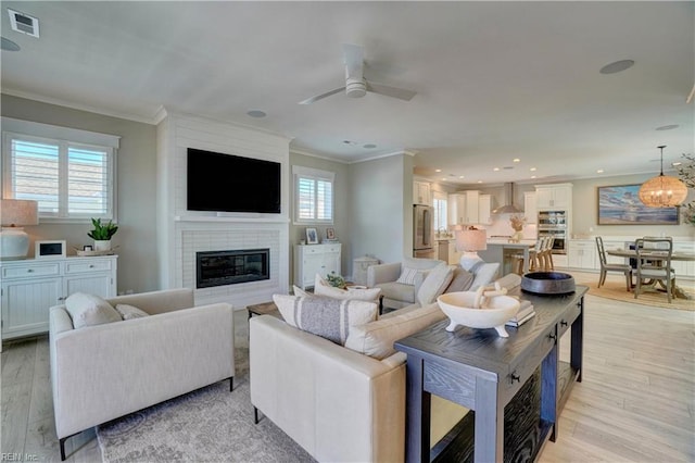 living room featuring a large fireplace, ornamental molding, light wood-style flooring, and visible vents