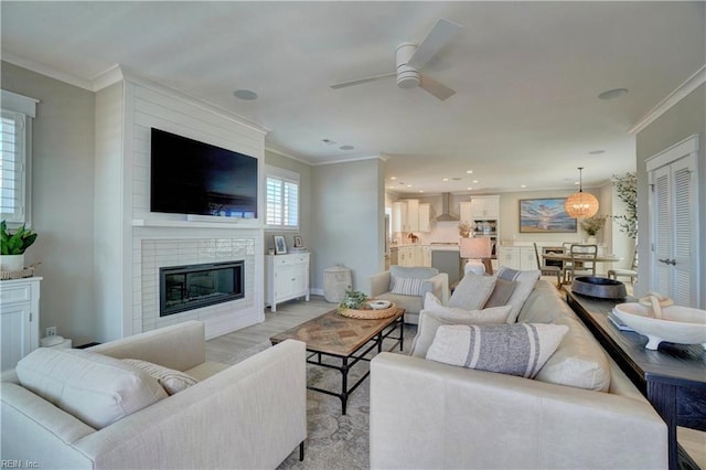 living area featuring crown molding, a fireplace, a ceiling fan, recessed lighting, and light wood-type flooring