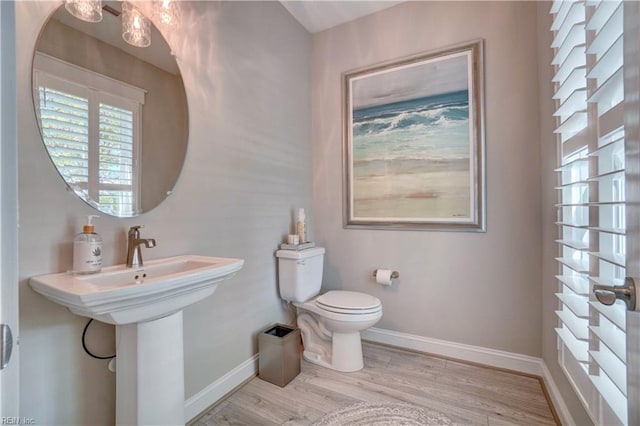 half bath with toilet, baseboards, and wood finished floors