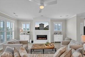 living room featuring crown molding, a warm lit fireplace, and a wealth of natural light