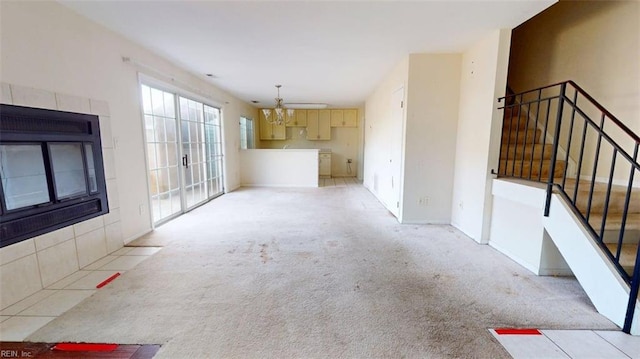 unfurnished living room featuring a chandelier, stairway, and light colored carpet