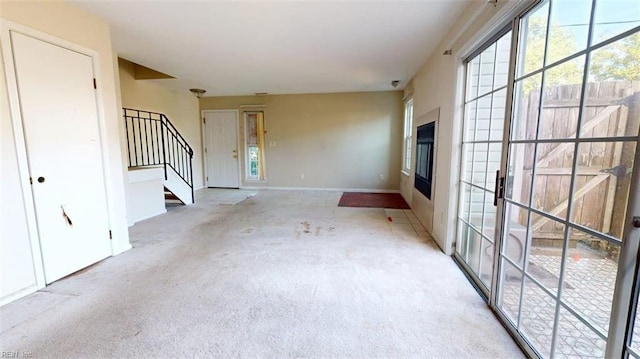 unfurnished living room featuring carpet floors, stairway, and baseboards
