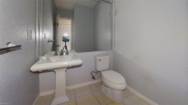 bathroom with tile patterned floors, toilet, a textured wall, and baseboards