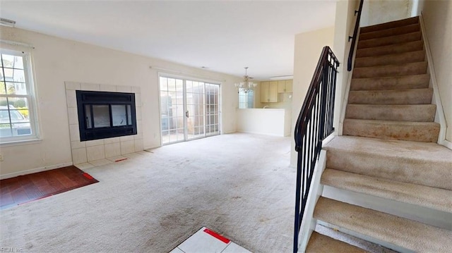 staircase with carpet flooring, healthy amount of natural light, a chandelier, and a tiled fireplace