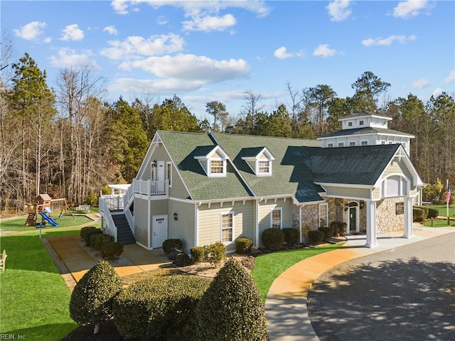 view of front facade with stone siding, a front yard, a shingled roof, a playground, and stairway