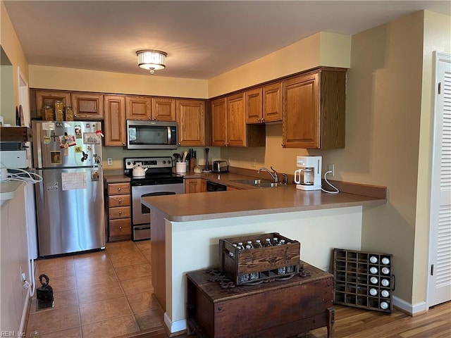 kitchen featuring appliances with stainless steel finishes, a sink, brown cabinetry, a peninsula, and baseboards