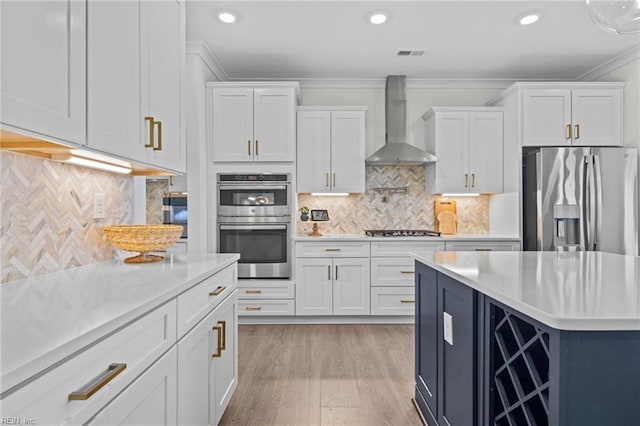 kitchen featuring light countertops, appliances with stainless steel finishes, wall chimney exhaust hood, and white cabinetry