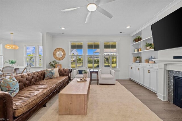 living area with crown molding, ceiling fan, a fireplace, and wood finished floors