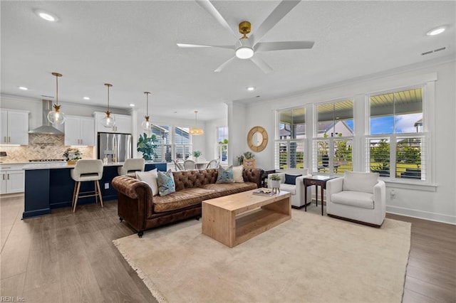 living room featuring ceiling fan, recessed lighting, wood finished floors, visible vents, and ornamental molding