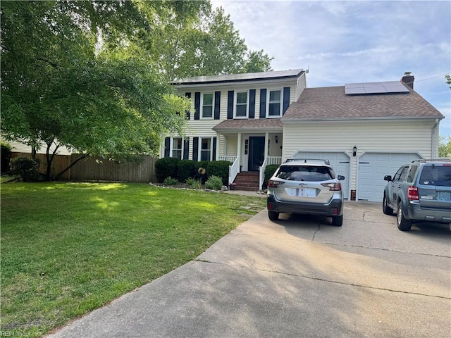 colonial house with a garage, fence, a front yard, roof mounted solar panels, and concrete driveway