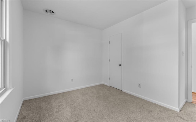 spare room featuring baseboards, light colored carpet, and visible vents