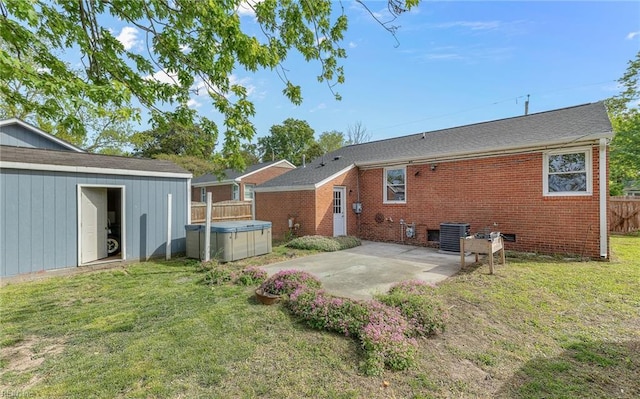 rear view of property with a patio area, a hot tub, brick siding, fence, and a yard