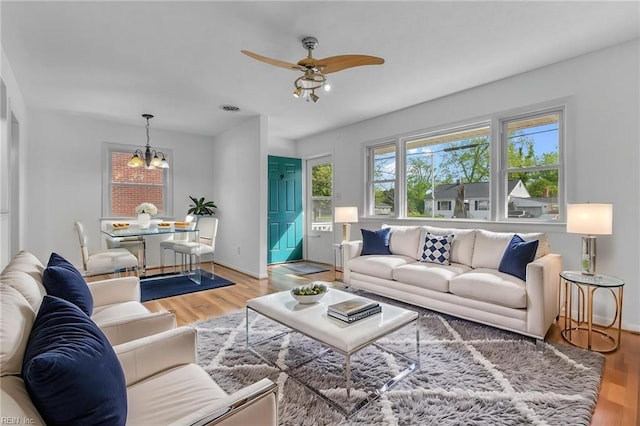 living area featuring baseboards, ceiling fan with notable chandelier, and wood finished floors