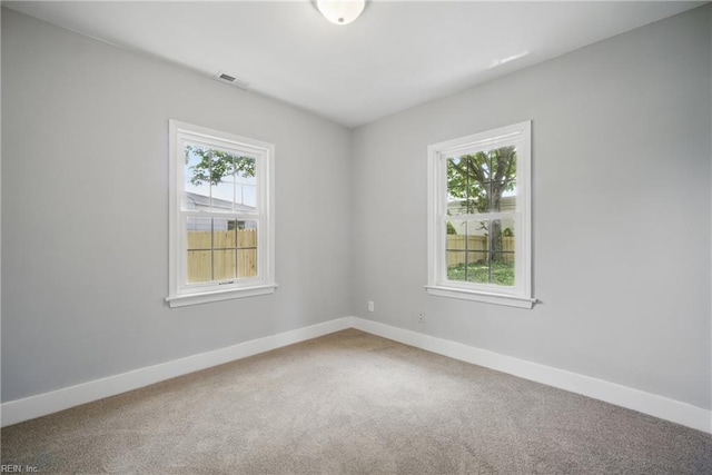 carpeted spare room with a healthy amount of sunlight, baseboards, and visible vents