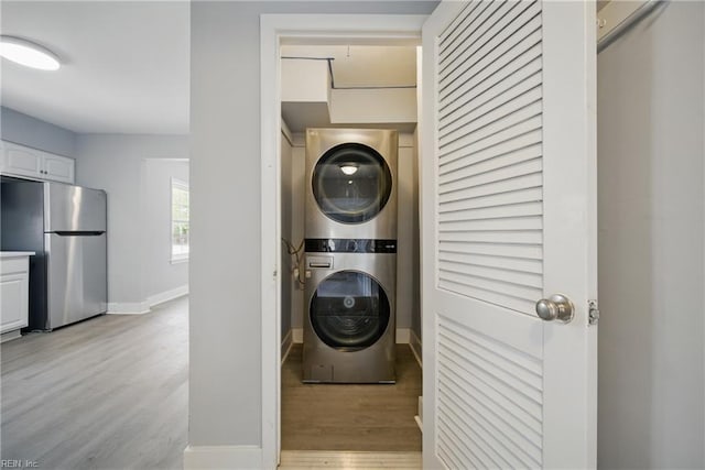 washroom with baseboards, laundry area, stacked washer and clothes dryer, and light wood-type flooring