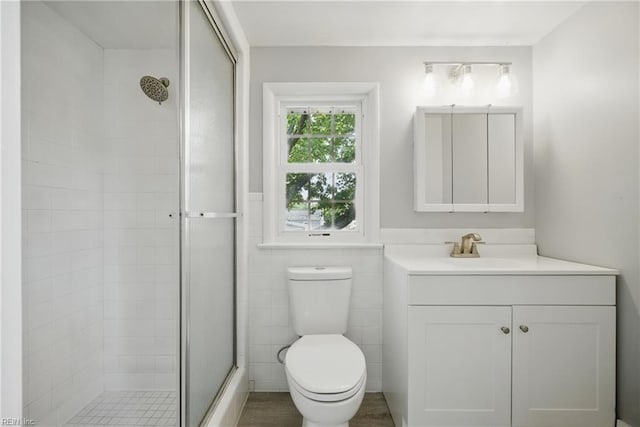 full bathroom with vanity, a stall shower, toilet, and tile walls