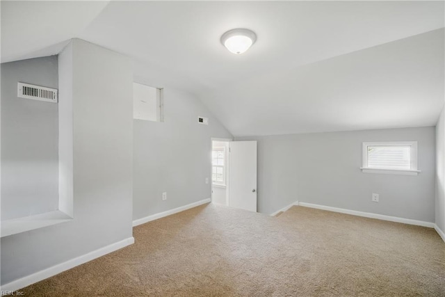 additional living space featuring visible vents, baseboards, lofted ceiling, carpet flooring, and a wealth of natural light