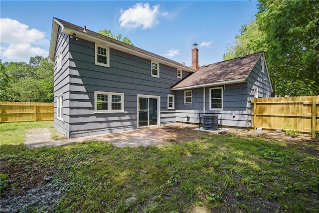 rear view of property with a fenced backyard, central AC unit, a chimney, a patio area, and a yard