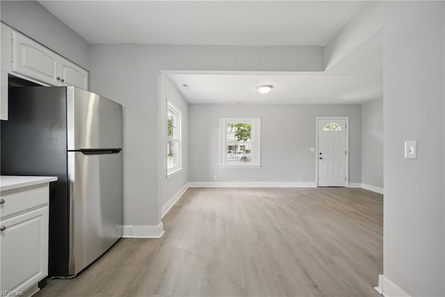 kitchen with white cabinets, light wood-style floors, light countertops, freestanding refrigerator, and baseboards