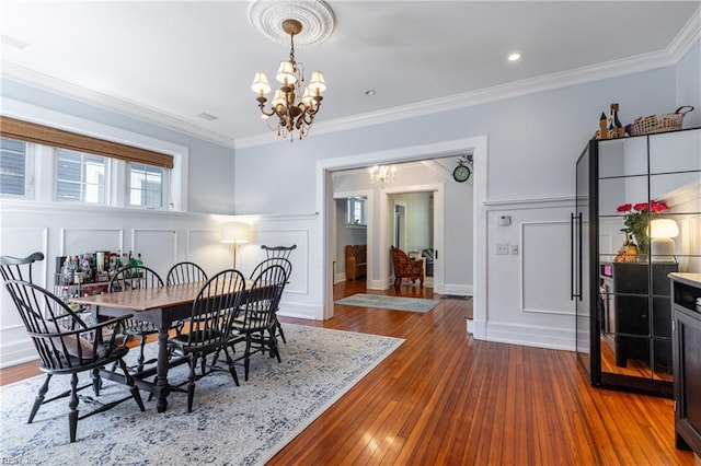 dining room with crown molding, a decorative wall, wood finished floors, and a chandelier