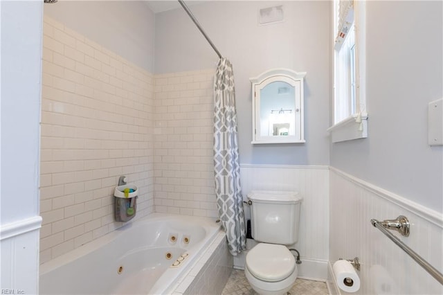 bathroom with toilet, a combined bath / shower with jetted tub, and a wainscoted wall