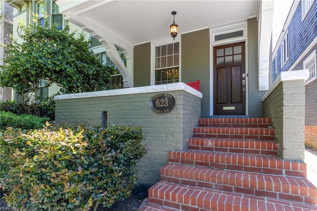 doorway to property featuring a porch and brick siding