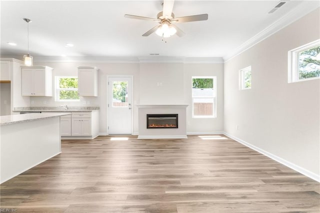unfurnished living room featuring ceiling fan, crown molding, baseboards, light wood finished floors, and a glass covered fireplace