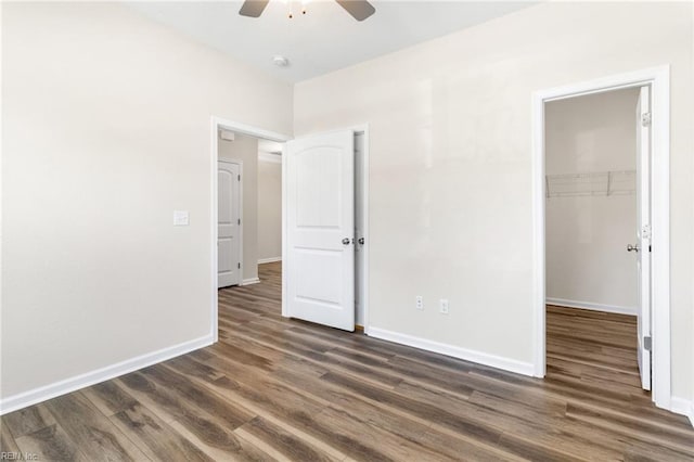 unfurnished bedroom featuring dark wood-type flooring, baseboards, a walk in closet, and a closet