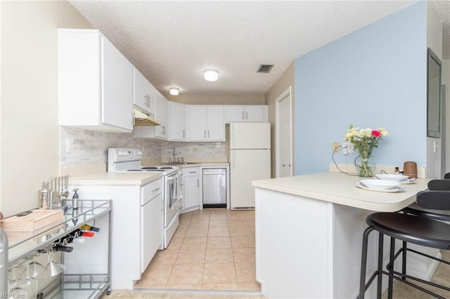 kitchen featuring visible vents, light countertops, a peninsula, under cabinet range hood, and white appliances