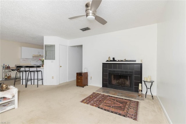 carpeted living room featuring visible vents, a ceiling fan, a textured ceiling, and a fireplace