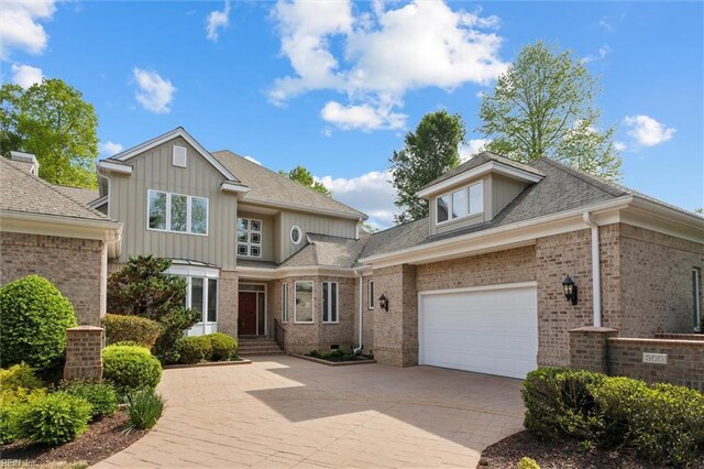 view of front of property with board and batten siding, brick siding, decorative driveway, and a garage