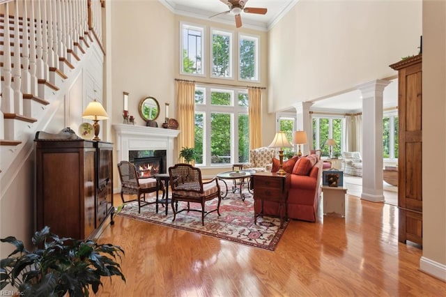 living area featuring ornate columns, a glass covered fireplace, crown molding, and wood finished floors