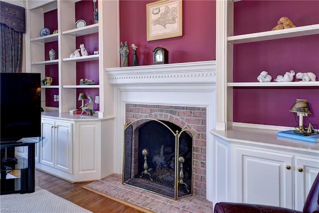 living area featuring a brick fireplace, wood finished floors, and built in shelves