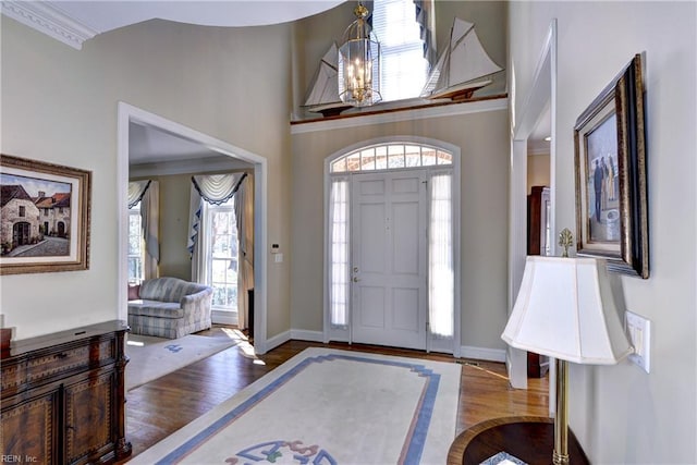 foyer with baseboards, a high ceiling, ornamental molding, and wood finished floors