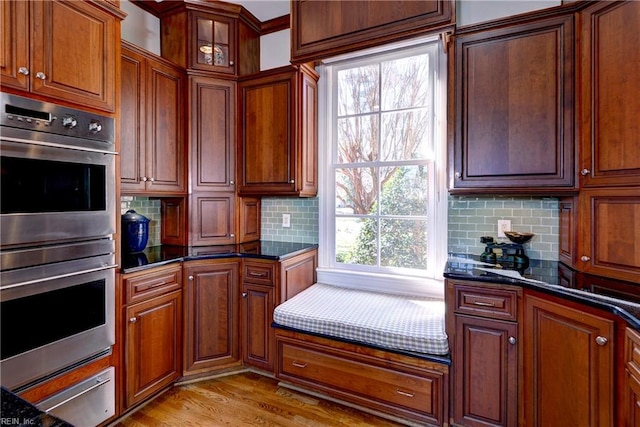 kitchen with dark stone countertops, tasteful backsplash, stainless steel double oven, and light wood-style flooring