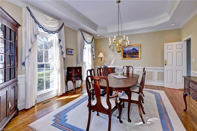 dining space with a healthy amount of sunlight, a raised ceiling, wood finished floors, and a notable chandelier