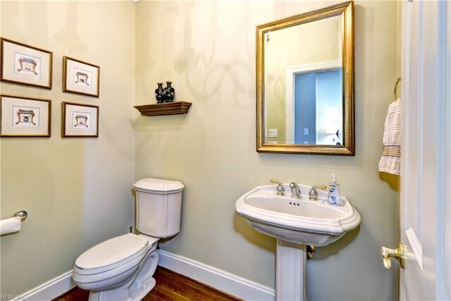 half bath with toilet, baseboards, and wood finished floors