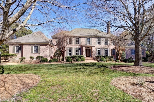 view of front of property with brick siding, a front lawn, and a chimney