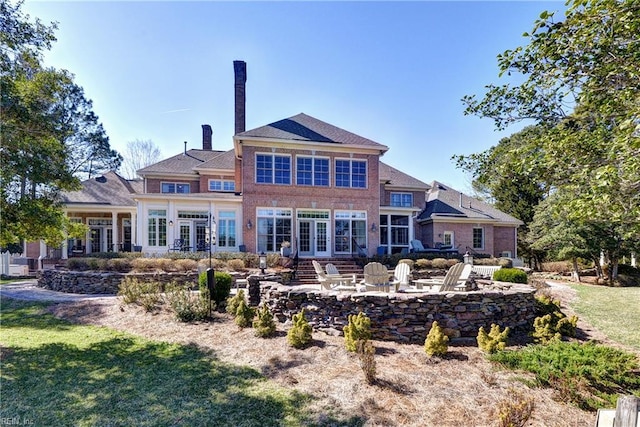 rear view of house featuring french doors, a chimney, brick siding, a patio area, and a lawn