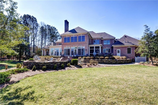 rear view of property featuring a chimney, a yard, and brick siding
