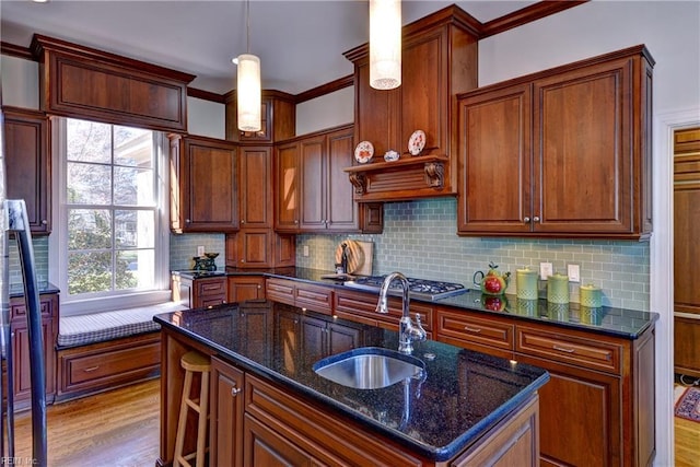 kitchen featuring tasteful backsplash, a center island with sink, a sink, light wood-style floors, and dark stone counters