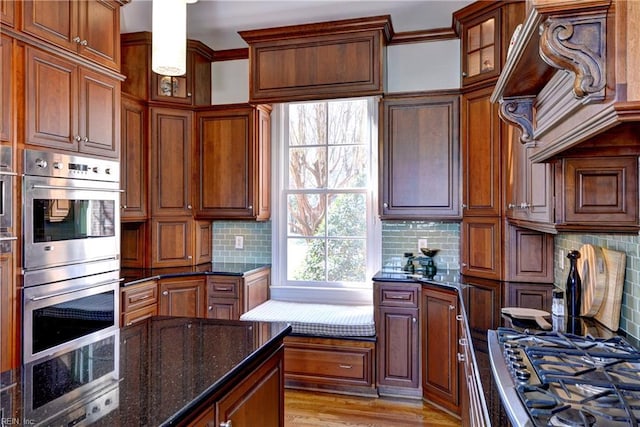kitchen featuring backsplash, brown cabinets, dark stone countertops, light wood-style floors, and stainless steel appliances