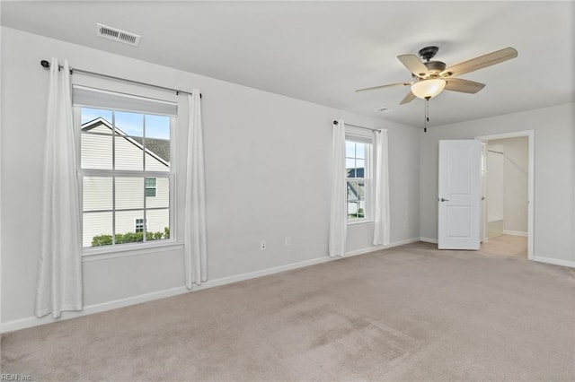 spare room featuring visible vents, ceiling fan, a wealth of natural light, and light carpet