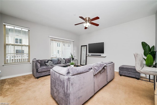 living area featuring baseboards, plenty of natural light, a ceiling fan, and light colored carpet