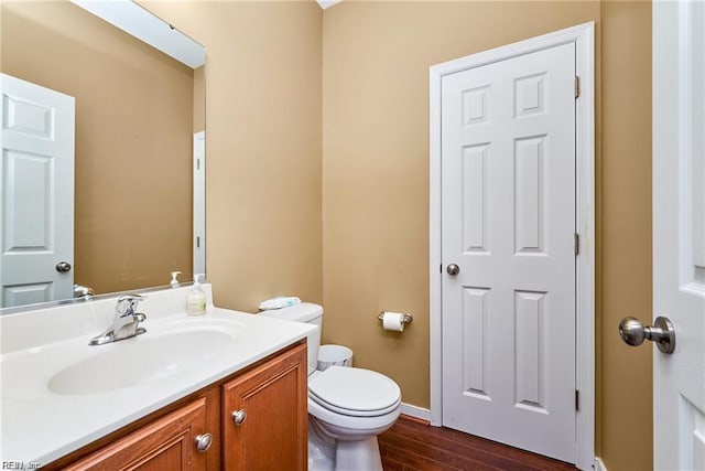 half bath with vanity, baseboards, toilet, and wood finished floors