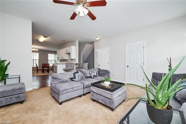 living room featuring baseboards, light colored carpet, and ceiling fan with notable chandelier