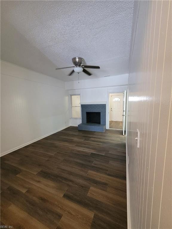 unfurnished living room featuring dark wood-style flooring, a fireplace with raised hearth, a textured ceiling, and ceiling fan