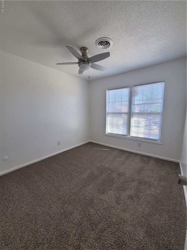 spare room featuring visible vents, baseboards, dark carpet, ceiling fan, and a textured ceiling