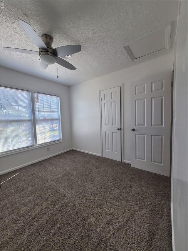 unfurnished bedroom featuring a ceiling fan, attic access, a textured ceiling, baseboards, and carpet flooring